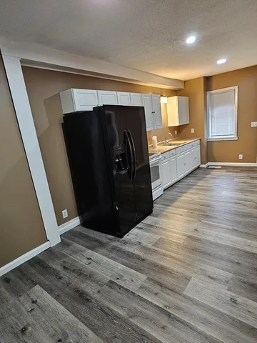 a view of a refrigerator in kitchen and an empty room with wooden floor