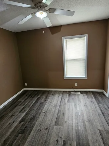 an empty room with wooden floor chandelier fan and windows