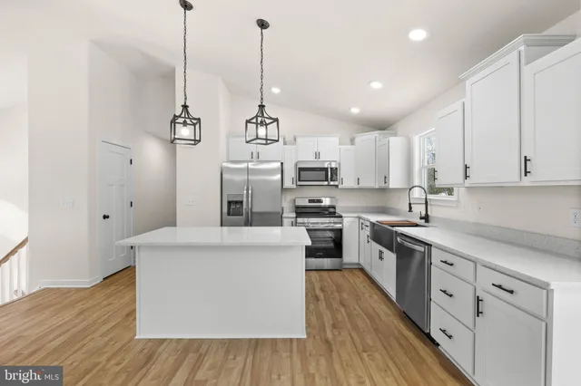 a large kitchen with stainless steel appliances granite countertop a sink a stove a refrigerator and white cabinets with wooden floor