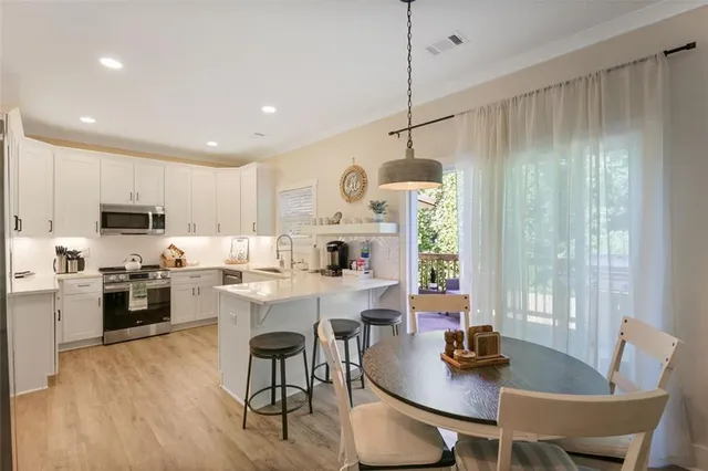 a kitchen with stainless steel appliances granite countertop a stove a sink a refrigerator a dining table and chairs with wooden floor