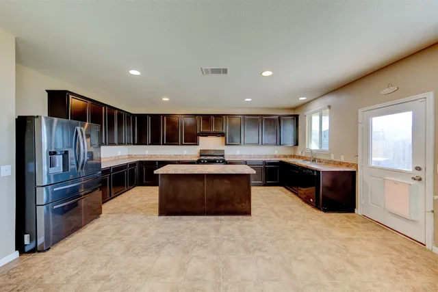 a kitchen with stainless steel appliances kitchen island granite countertop a stove a sink a refrigerator and a cabinets