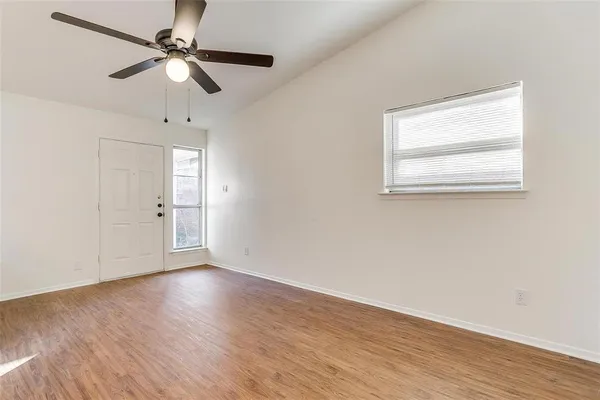 an empty room with wooden floor fan and windows