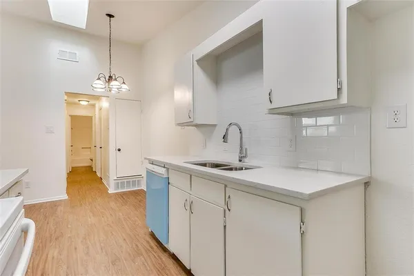 a kitchen with a sink dishwasher and white cabinets with wooden floor