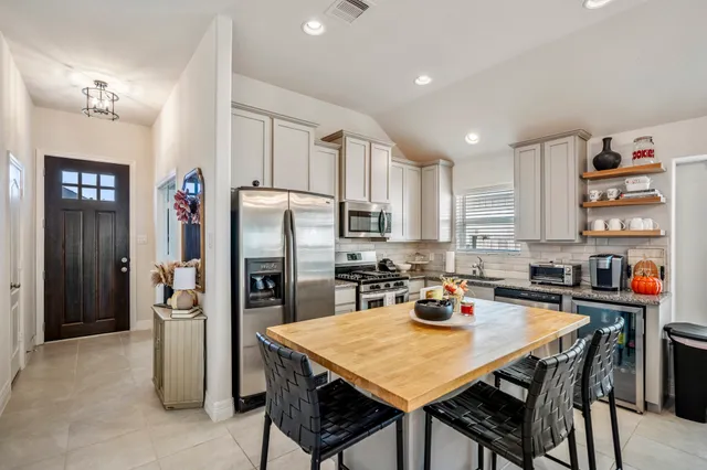 a kitchen with stainless steel appliances granite countertop a dining table chairs refrigerator and sink