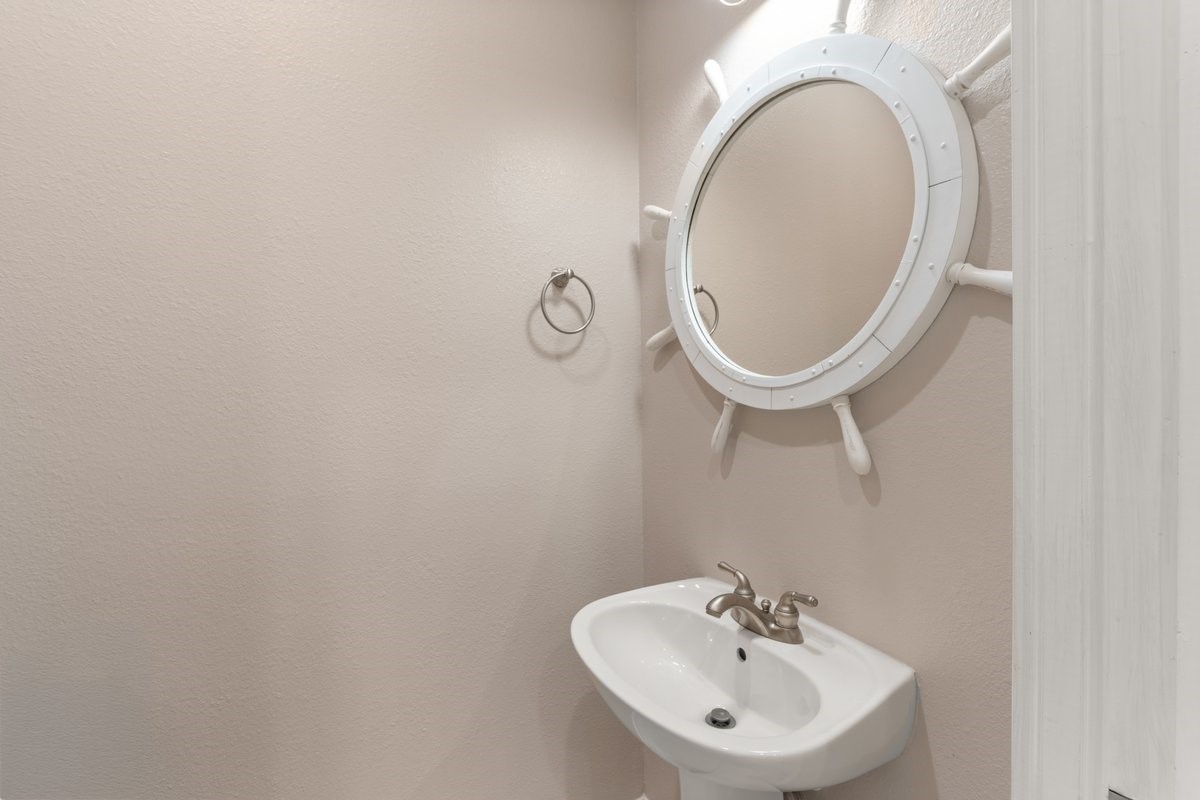 168 Lake Point Boulevard, Unit C102 Conroe, TX 77356 - Photo 25 of 35 Compact powder room with a nautical-themed mirror and a sleek pedestal sink. Neutral walls create a clean, simple aesthetic.