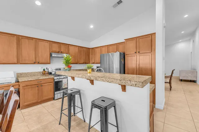 a kitchen with stainless steel appliances granite countertop a refrigerator a stove a sink a dining table and chairs with wooden floor