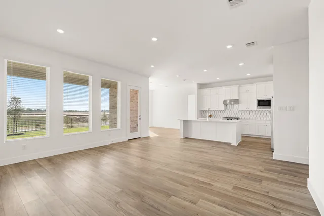 a view of an empty room with wooden floor and a kitchen