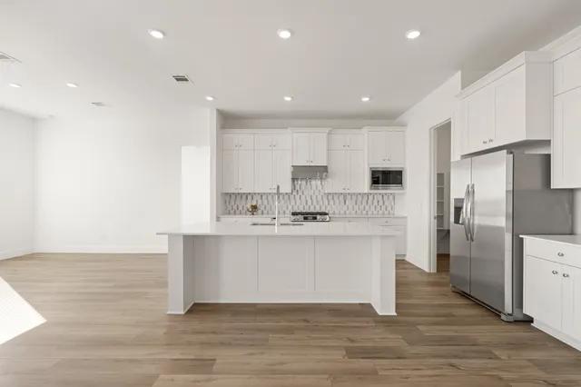 a large white kitchen with kitchen island a sink stainless steel appliances and cabinets