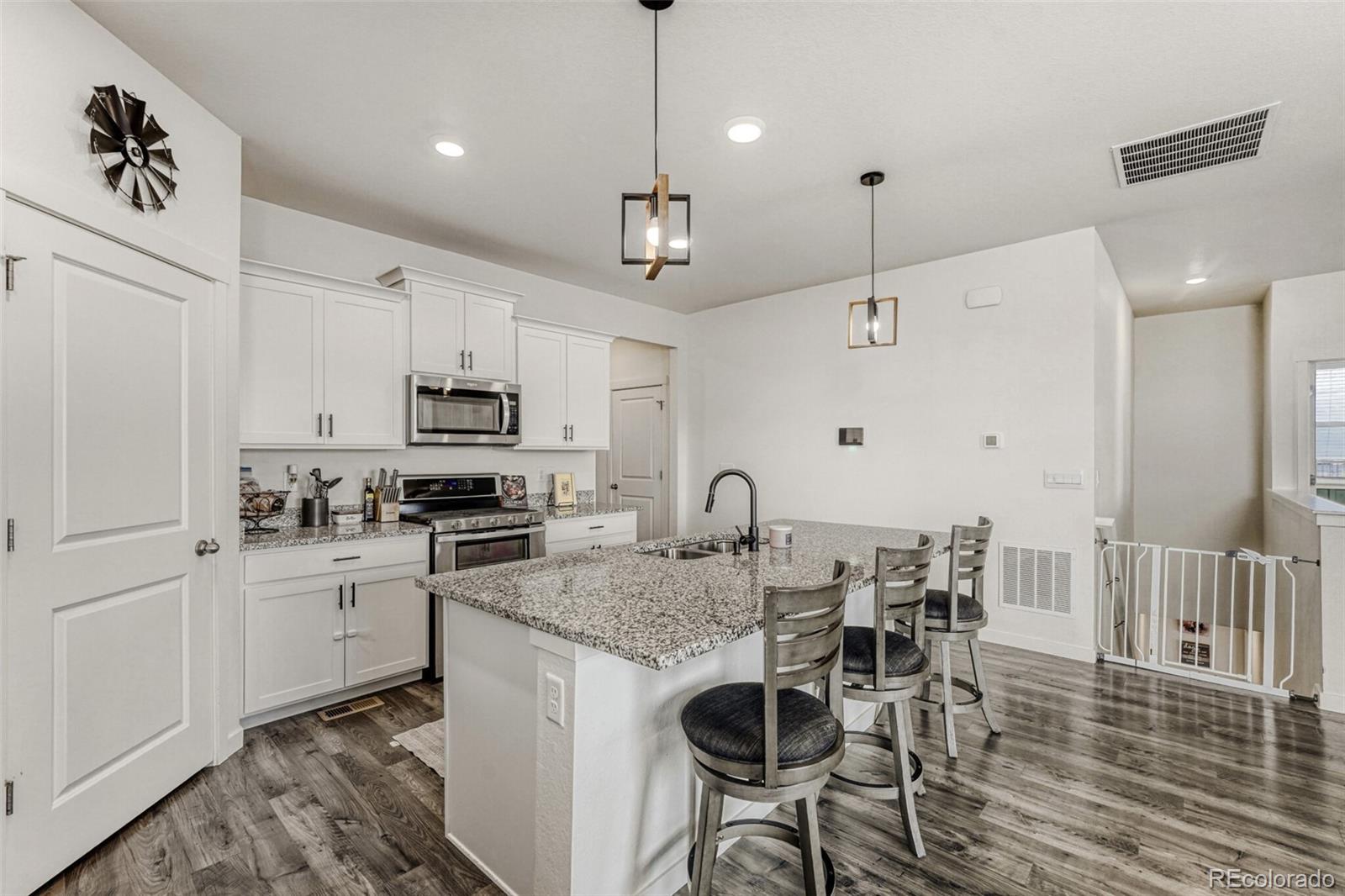 166 Racer Street Bennett, CO 80102 - Photo 11 of 44 a kitchen with stainless steel appliances granite countertop a stove top oven a refrigerator a sink and a dining table with wooden floor