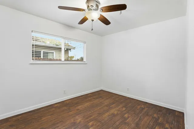 an empty room with wooden floor ceiling fan and windows