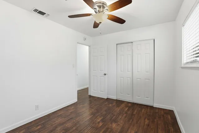 an empty room with wooden floor chandelier fan and windows