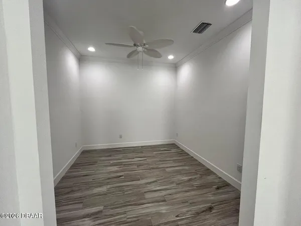 a view of an empty room with wooden floor and fan