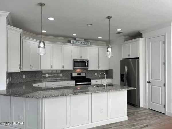 a kitchen with kitchen island granite countertop a refrigerator a stove a sink and white cabinets