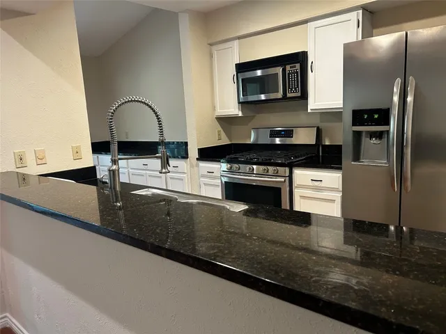 a kitchen with stainless steel appliances granite countertop a sink a stove and a refrigerator with wooden floor