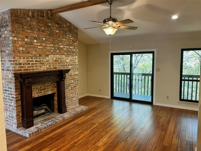 a view of an empty room with wooden floor fireplace and a window