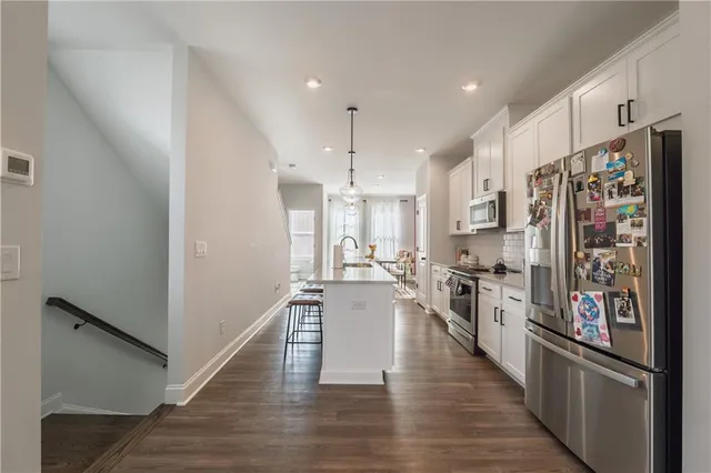 a kitchen with stainless steel appliances a stove top oven a refrigerator a sink and white cabinets with wooden floor