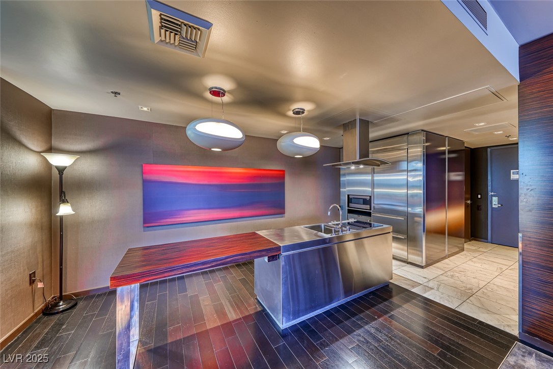 4381 West Flamingo Road, Unit 901 Las Vegas, NV 89103 - Photo 7 of 58 Kitchen featuring stainless steel countertops, a sink, island exhaust hood, stainless steel microwave, and wood finished floors