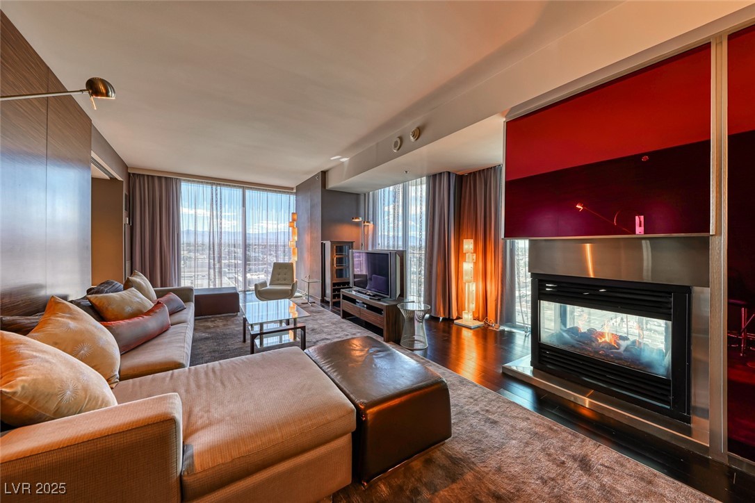 4381 West Flamingo Road, Unit 901 Las Vegas, NV 89103 - Photo 9 of 58 Living area with a multi sided fireplace, expansive windows, and wood finished floors
