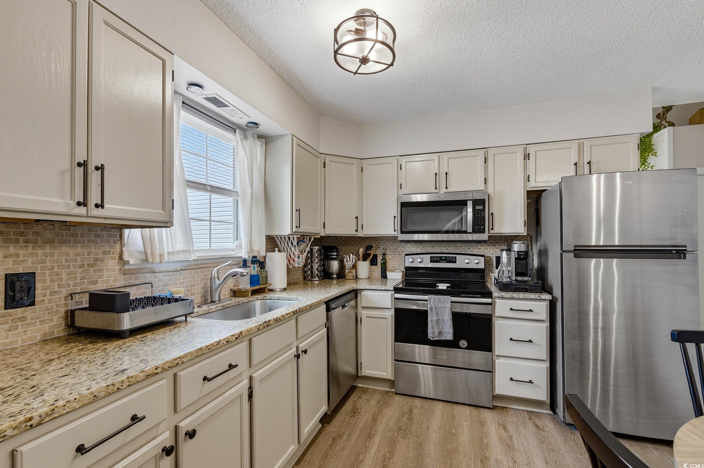 418 Chesterfield Court Myrtle Beach, SC 29577 - Photo 5 of 18 Kitchen with appliances with stainless steel finishes, a textured ceiling, light stone counters, backsplash, and white cabinets
