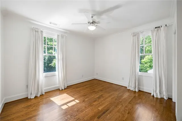 an empty room with wooden floor fan and windows