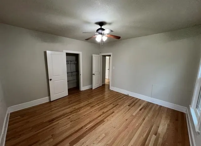 a view of an empty room with wooden floor and a ceiling fan
