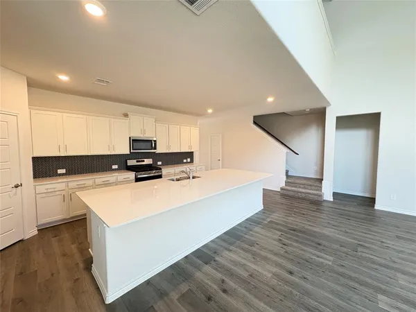 a large white kitchen with wooden floors stainless steel appliances and a refrigerator