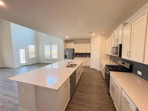 a large kitchen with stainless steel appliances a large counter top a stove a sink a refrigerator white cabinets and wooden floor
