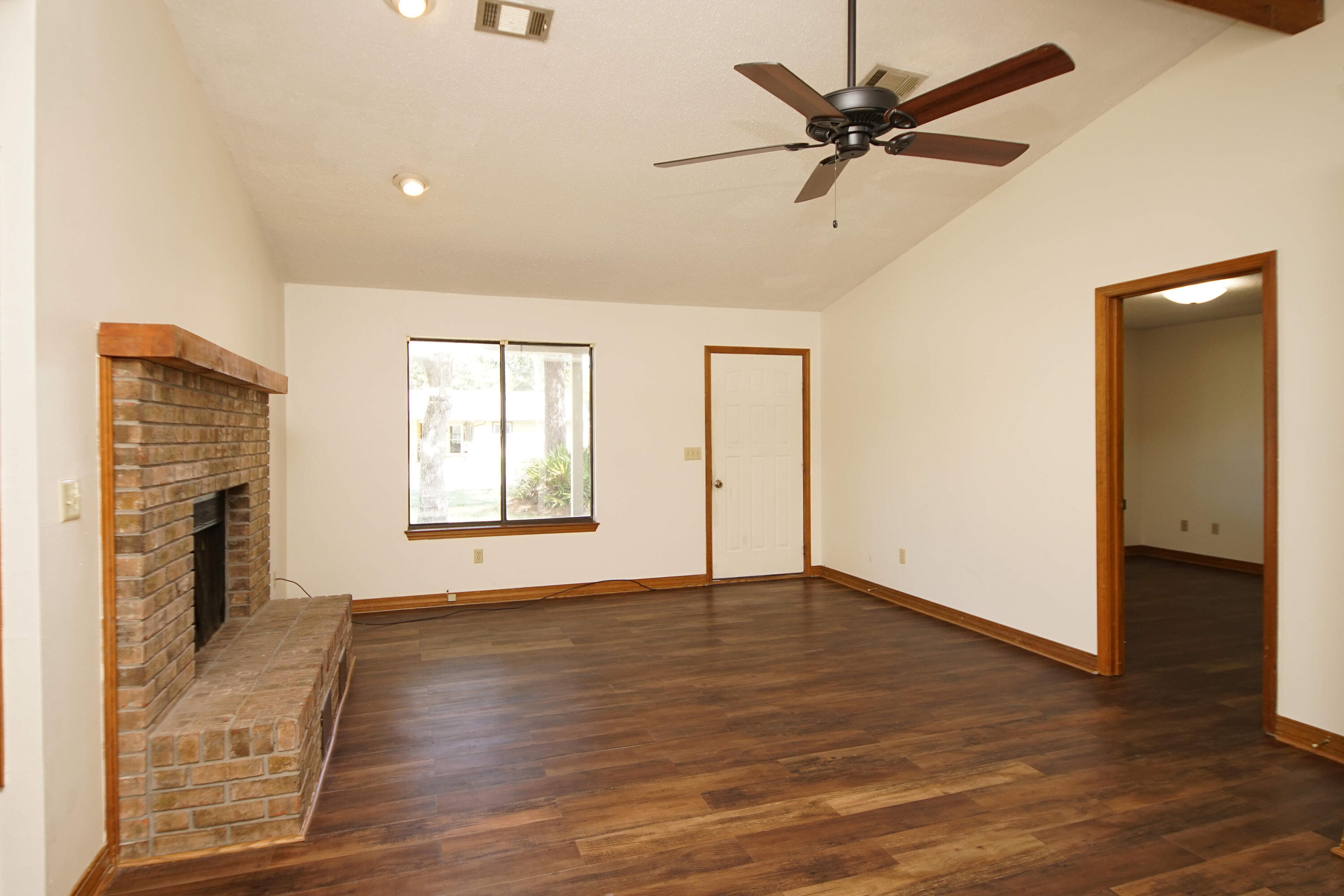 912 Nutmeg Avenue Niceville, FL 32578 - Photo 9 of 30 an empty room with wooden floor a ceiling fan and a fireplace