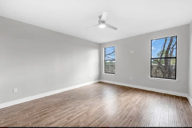 an empty room with wooden floor chandelier fan and windows