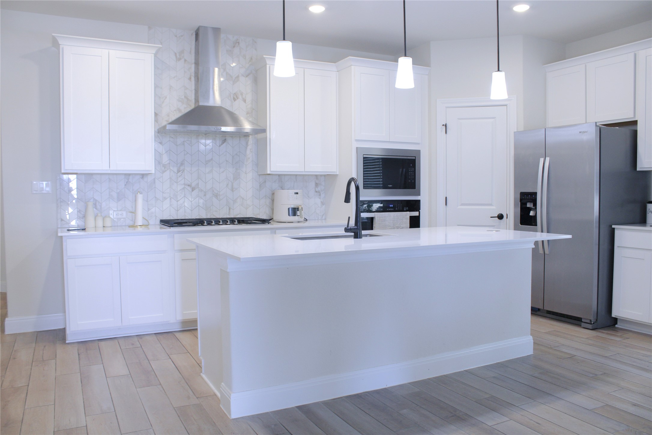 An open kitchen showcases a central island, shaker cabinets, and stone countertops.