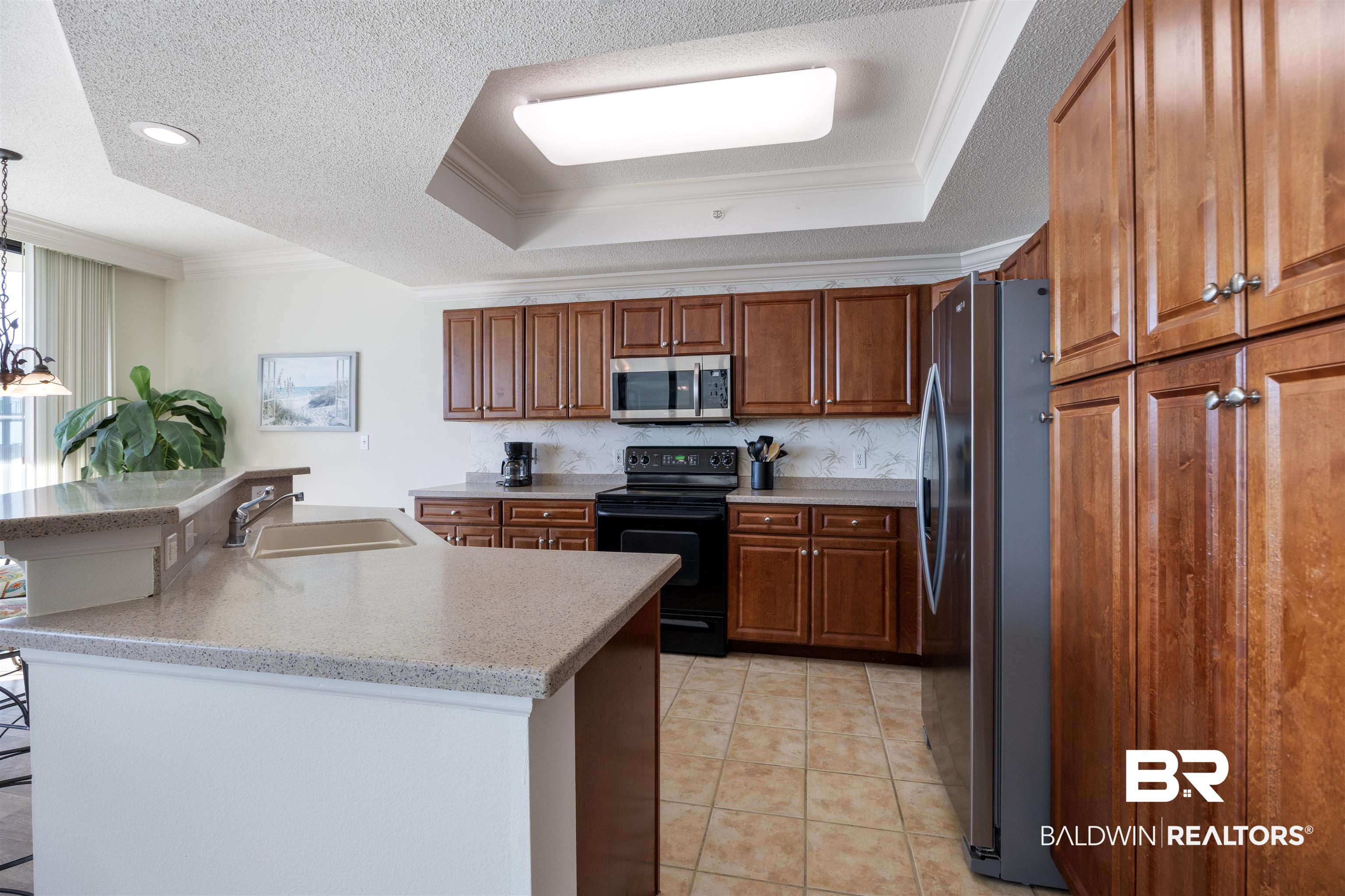27580 Canal Road, Unit 1431 Orange Beach, AL 36561 - Photo 16 of 73 Kitchen with ornamental molding, stainless steel appliances, a tray ceiling, brown cabinetry, and a center island with sink