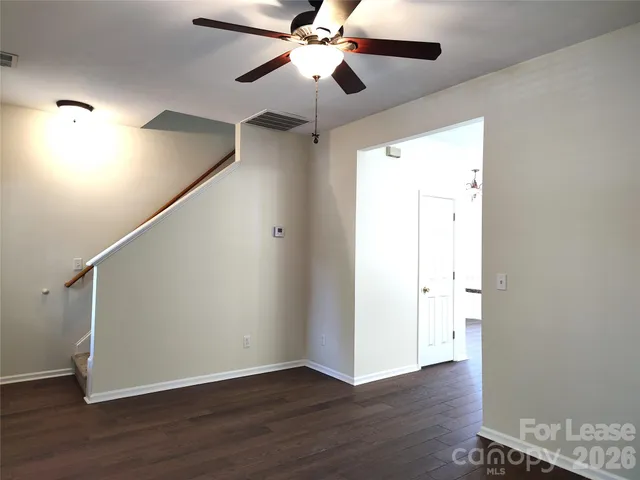 a view of an empty room with wooden floor and a ceiling fan