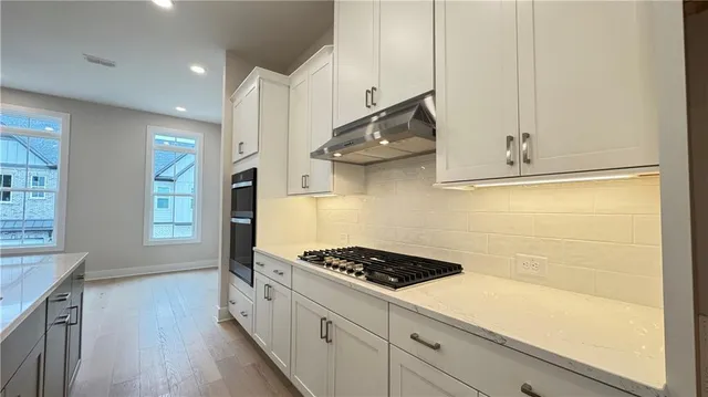 a large kitchen with granite countertop a large kitchen island white cabinetry and stainless steel appliances
