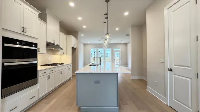 a kitchen with stainless steel appliances granite countertop a refrigerator a sink a stove and white cabinets with wooden floor