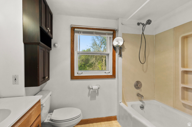 658 North 100 East Logan, UT 84321 - Photo 15 of 26 Bathroom featuring a full tub with an integrated shower, built-in storage shelving, dark wood-finish cabinetry, a window with natural light, and a toilet