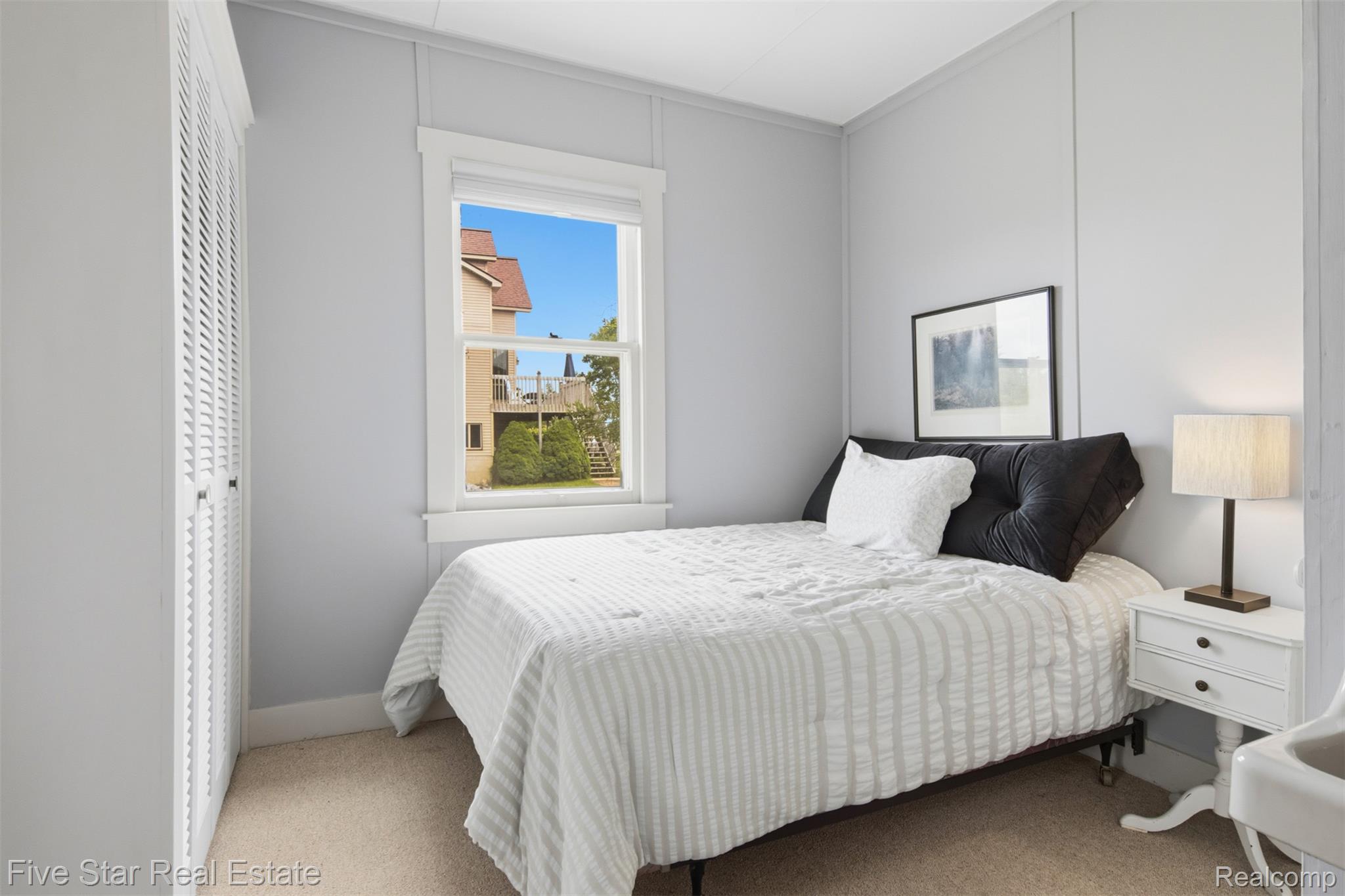 2588 Lakeview Road Onekama, MI 49675 - Photo 18 of 32 Bedroom featuring a single window, neutral wall paneling, light-toned carpet, and a built-in louvered closet
