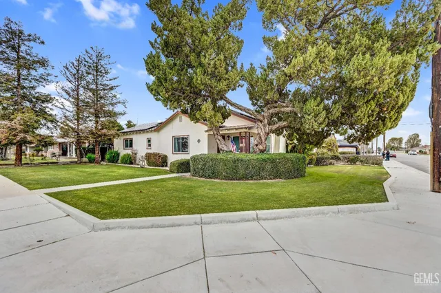 a view of a white house next to a yard with big trees