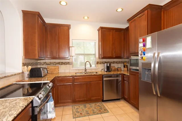 a kitchen with stainless steel appliances granite countertop a sink a stove a refrigerator cabinets and a window