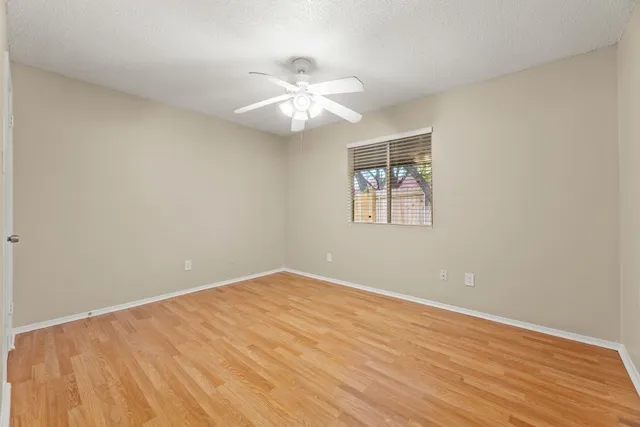 an empty room with wooden floor chandelier fan and windows