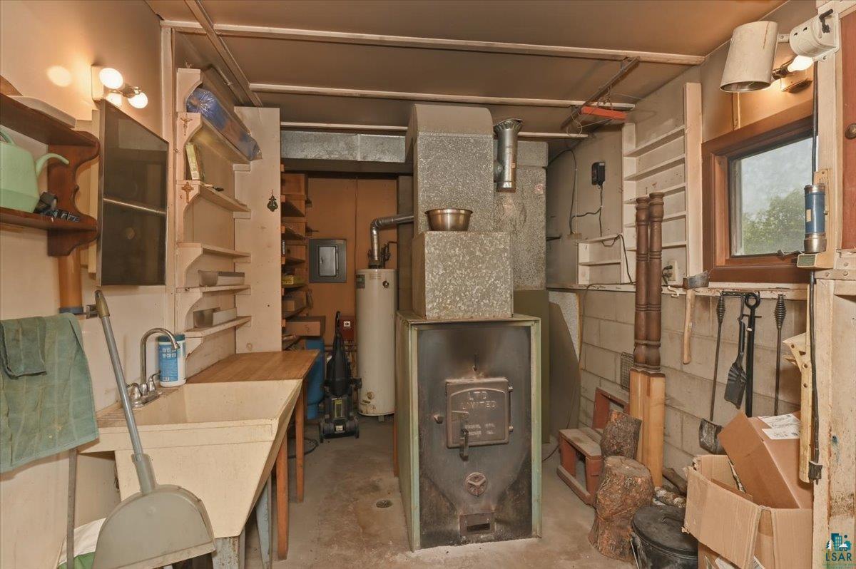 5190 County Road M Gordon, WI 54838 - Photo 20 of 31 Utility room featuring a large utility sink with a wood-finish countertop, adjacent built-in shelving, a wood-burning stove with a flue, and a visible water heater