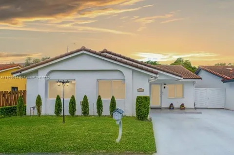 a view of a white house with a big yard and potted plants