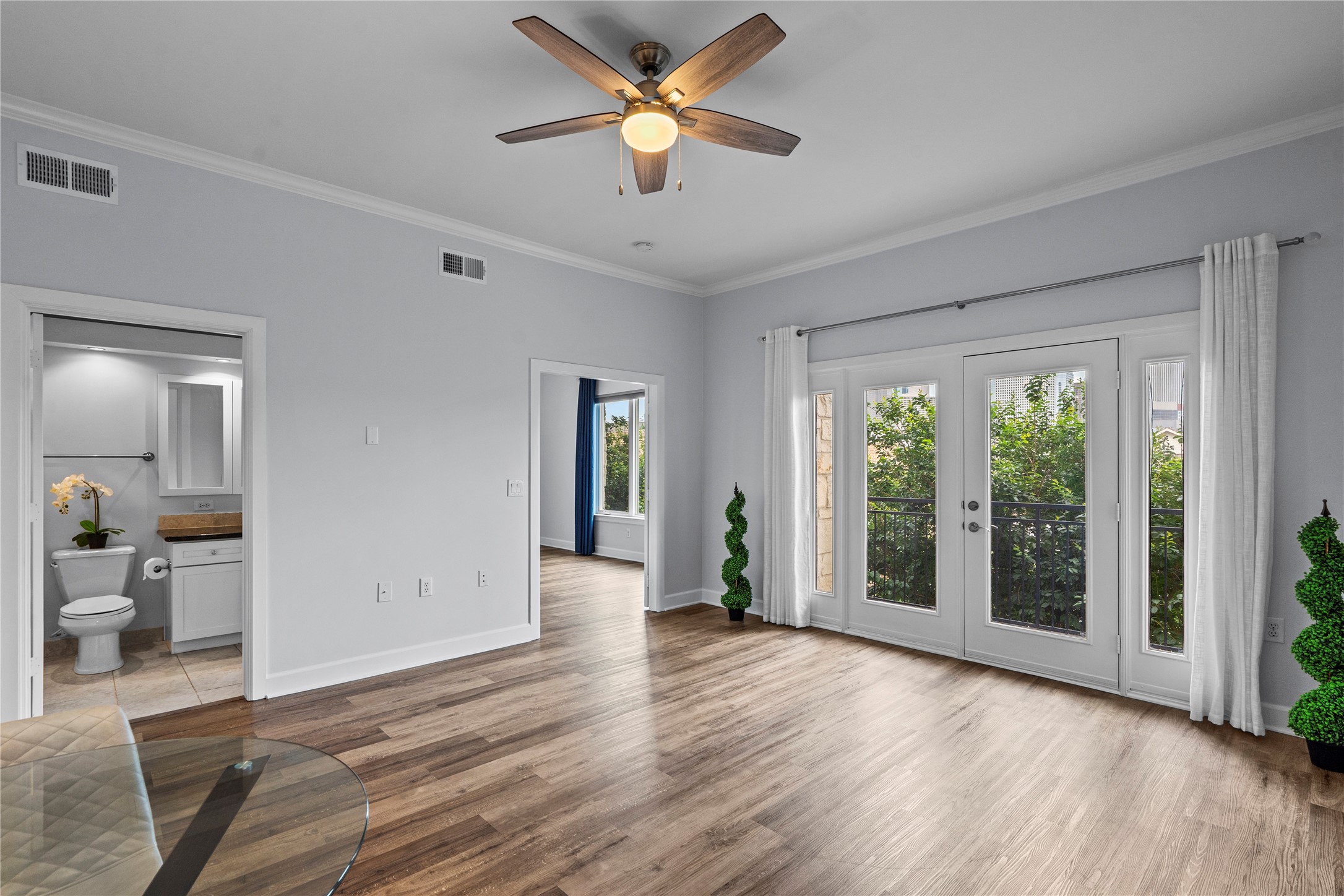 1900 Genesee Street, Unit 203 Houston, TX 77006 - Photo 4 of 30 Bright, open living space with wood flooring, ceiling fan, and French doors leading to a balcony. Adjacent bathroom and additional room offer convenience and versatility.
