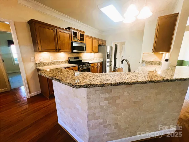 a kitchen with granite countertop a sink a stove top oven a refrigerator and wooden floors