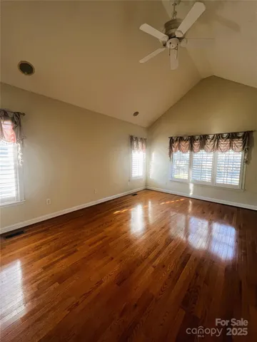 an empty room with wooden floor fan and windows