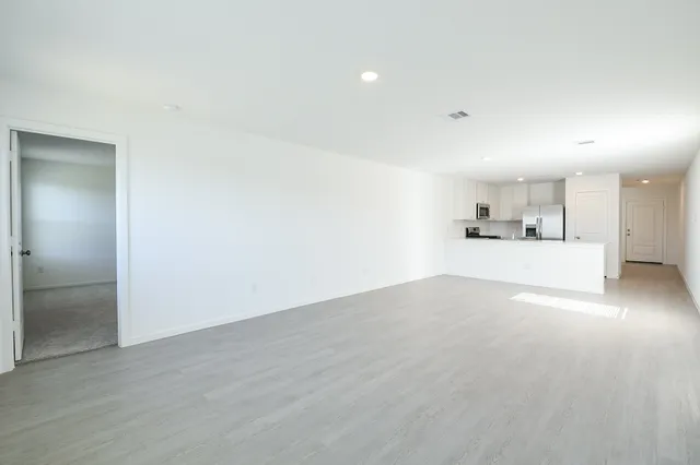 an empty room with wooden floor and a kitchen