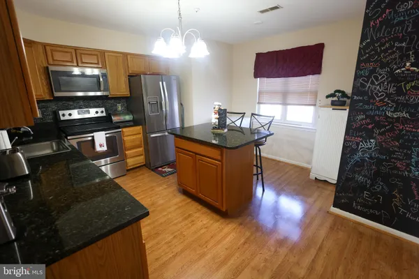 a kitchen with stainless steel appliances granite countertop a stove top oven a sink dishwasher and a refrigerator with wooden floor