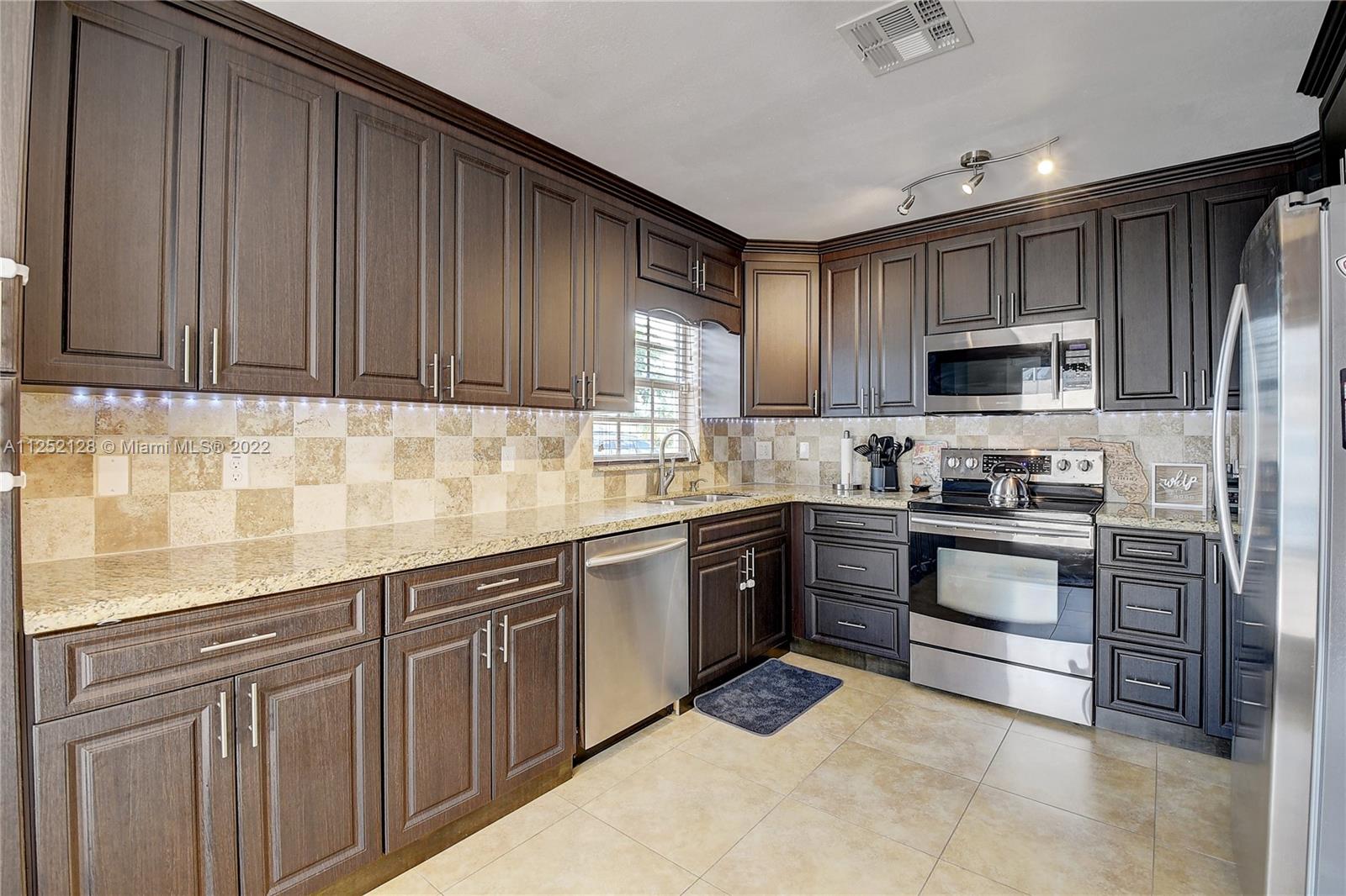 Boca Gardens Boca Raton, FL 33496 - Photo 5 of 19 a kitchen with granite countertop wooden cabinets a stove top oven and stainless steel appliances