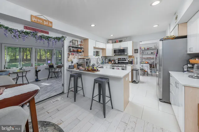 a living room with stainless steel appliances furniture a rug kitchen view and a large window