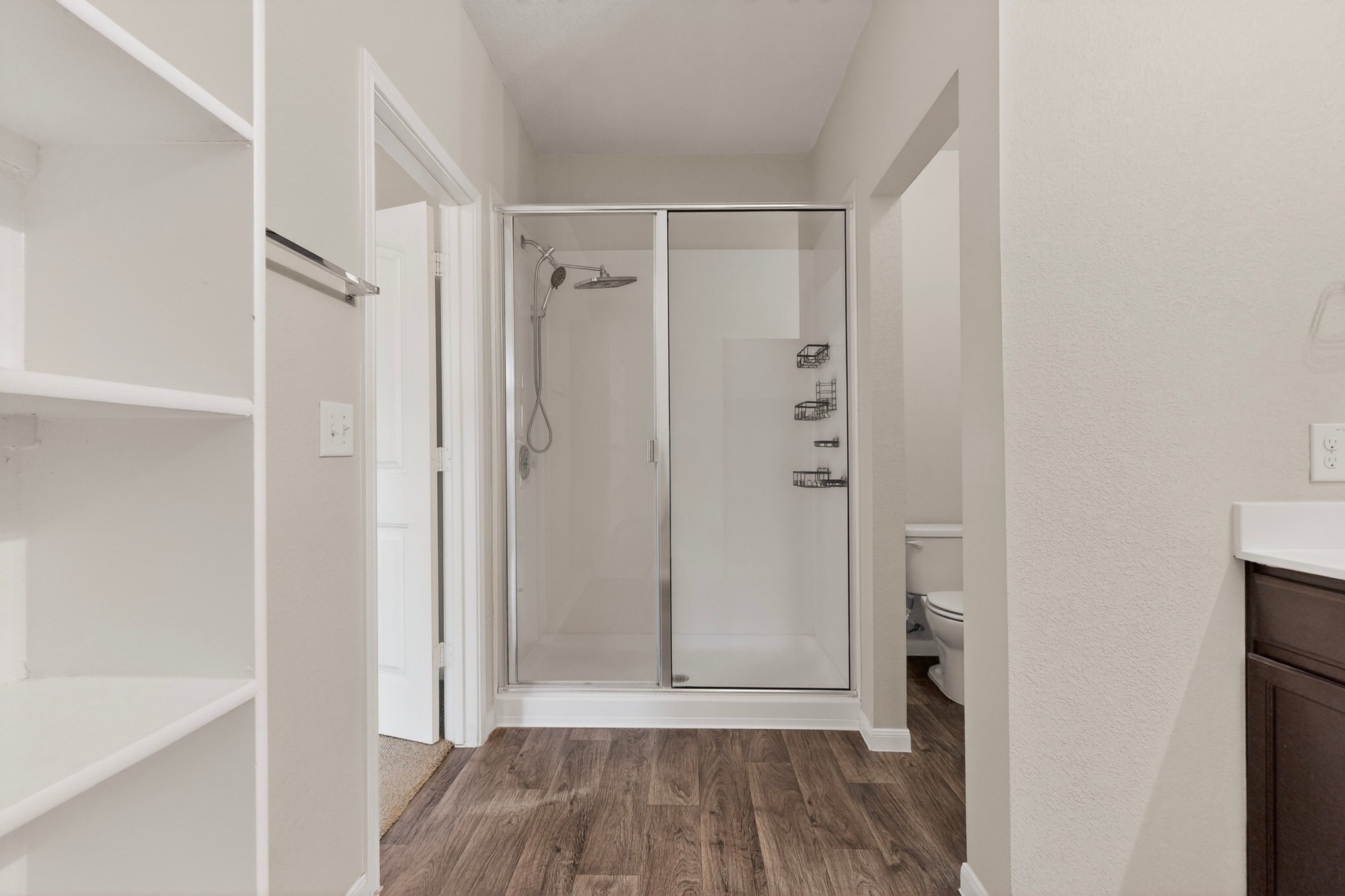 5905 Diamondleaf Bend Austin, TX 78724 - Photo 20 of 38 Enclosed shower with glass doors and built-in shelving, wood-finish flooring, and light neutral wall paint