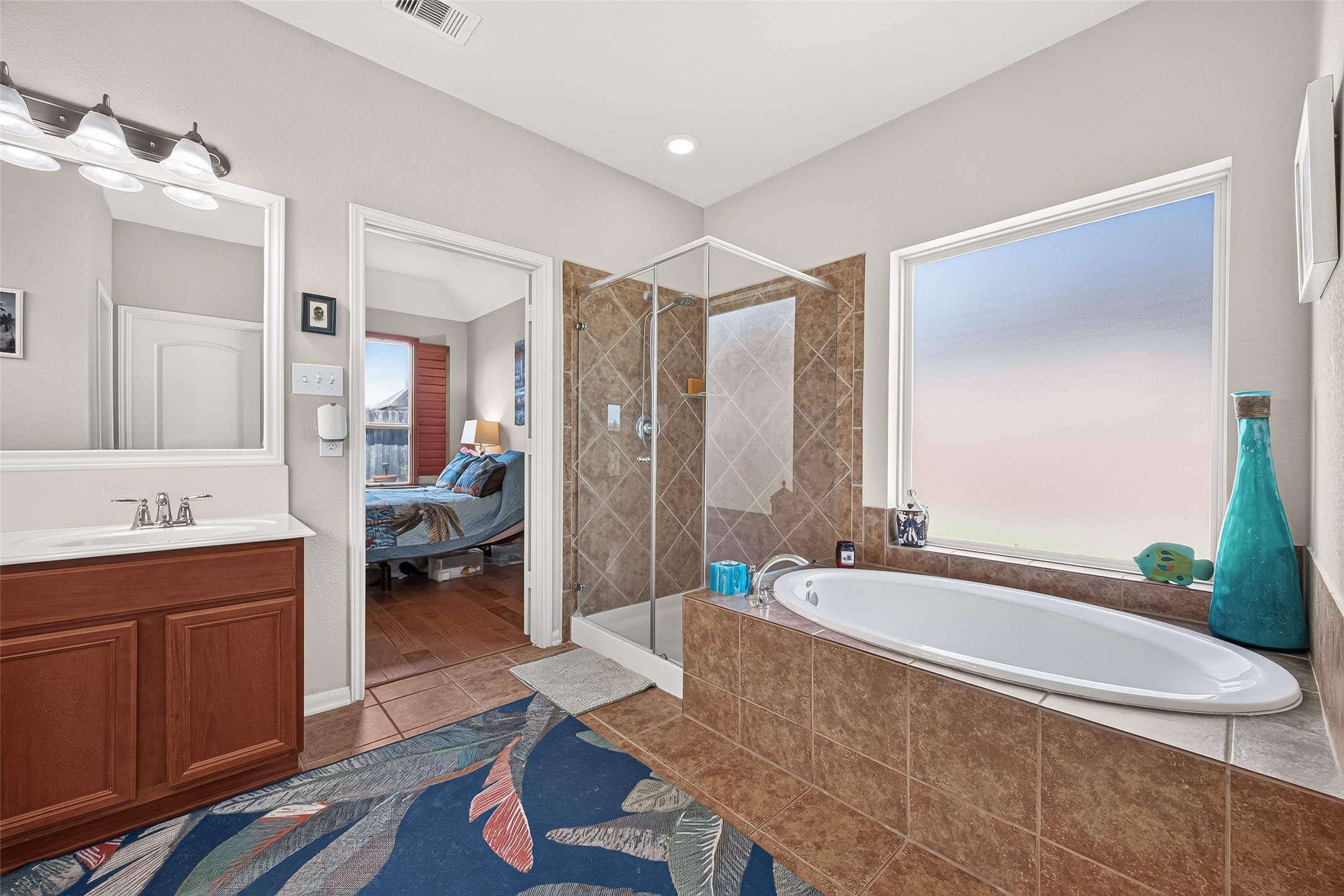 4910 Culver Lane Rosenberg, TX 77471 - Photo 29 of 50 The primary bathroom features a modern design with a spacious soaking tub, seamless glass-enclosed shower, and double vanity. Natural light streams through a large frosted window, creating a bright and inviting atmosphere.